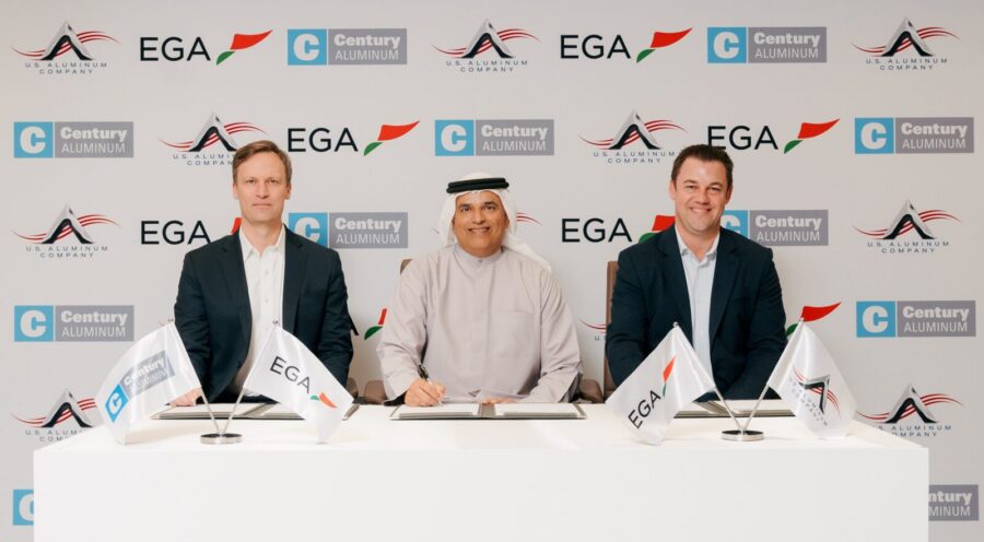 Three men sit at a table with documents, in front of a backdrop featuring EGA, Century Aluminum, and UAE Aluminium Company logos—highlighting Century Aluminum's new smelter project with EGA—with branded flags placed on the table.